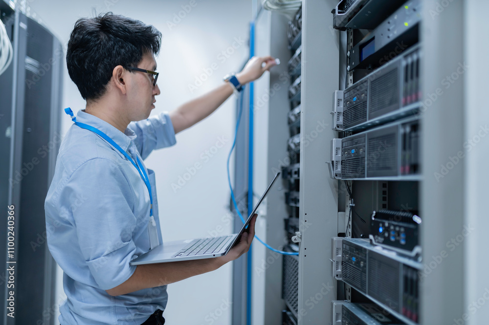 Fototapeta premium Computer engineer is setting up network in server room,Systems Maintenance Technician,Male engineer working in server room at modern data center