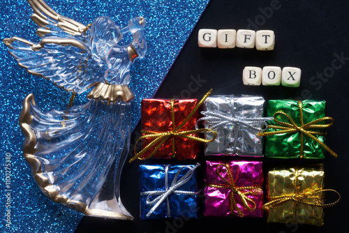 Multicolored gift boxes next to a Christmas souvenir - an angel with a trumpet and the inscription gift box. Photo. Top view. Selective focus photo