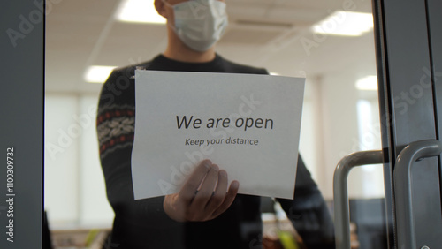 Business owner an attractive man in jumper changes the sign on photo