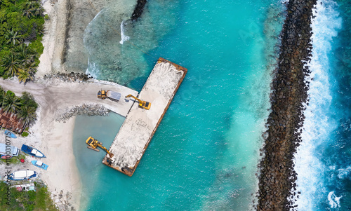 Aerial view of construction site with excavator near the harbour and pier, Fuvahmulah, Maldives. photo