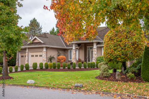 Fototapeta Naklejka Na Ścianę i Meble -  Two story stucco luxury house with garage door, big tree and nice Fall foliage landscape in Vancouver, Canada, North America. Day time on November 2024.