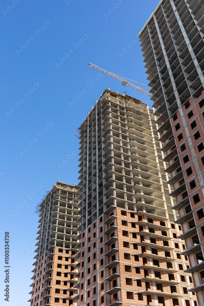 Obraz premium Three modern high-rise panel houses under construction and a tower crane against the blue sky, vertical photo.