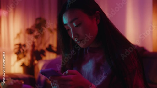 Asian Woman on Sofa in Living Room Engaged in Interaction with Her Phone in colourfull neon light 