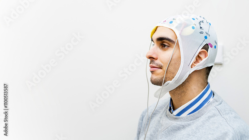 A young man undergoes transcranial direct current stimulation therapy for depressive disorders. The man is on a gray background. Copyspace for advertising.