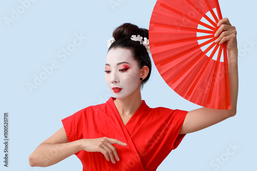 Beautiful young geisha with fan on light background photo