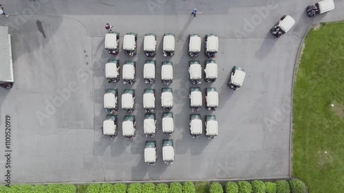 Birds-eye view of people getting into golf carts that sit in rows and slowly driving away from group in different directions. 