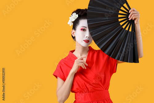 Beautiful young geisha with fan on yellow background photo