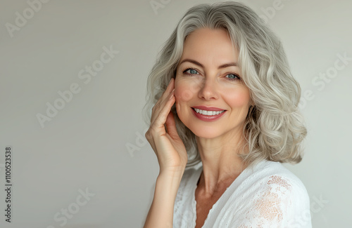 Adult elderly and beautiful woman 60 years old. Smiling charming woman with gray curly hair, touches her cheek. Beauty and care cosmetology for mature facial skin. Makeup and cosmetology