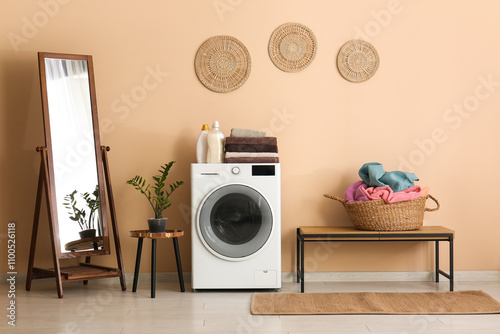 Modern washing machine, mirror, houseplant and basket with laundry in room photo