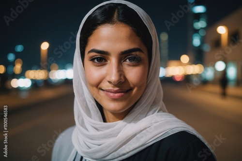 Close portrait of a smiling young Bahraini woman looking at the camera, Bahraini city outdoors at night blurred background photo