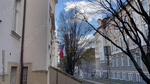 A postcardworthy urban scene features a striking white building, autumn tree, and a gently waving flag of Czech Republic, captured on smartphone. photo