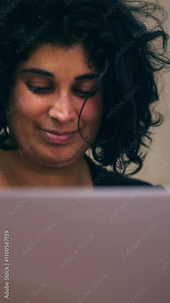 Vertical: A curly-haired girl with dark hair sits at her computer, writing a message on social media in her home, concentrating on her online interaction. Vertical: A curly-haired girl with dark hair sits at her computer, writing a message on social media in her home, concentrating on her online interaction.