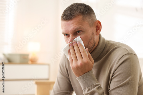 Man with tissue blowing runny nose at home. Space for text