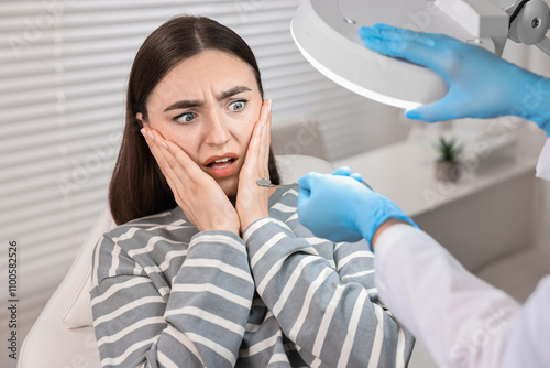 Dental phobia. Dentist working with scared woman in clinic, closeup photo