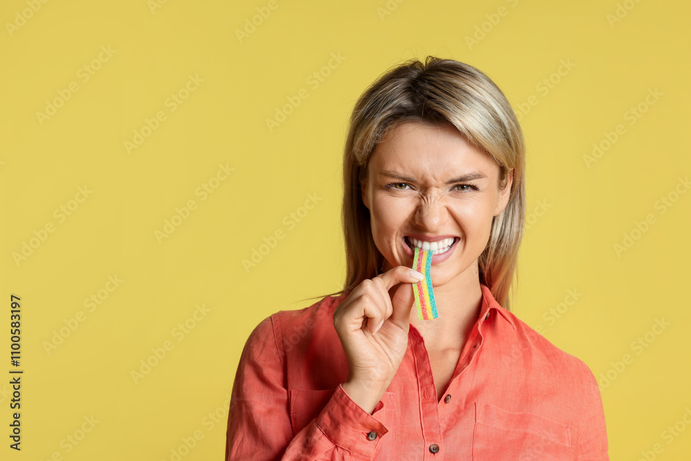 Young woman eating tasty rainbow sour belt on yellow background Young woman eating tasty rainbow sour belt on yellow background