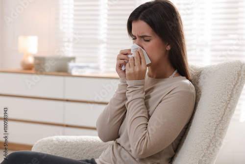 Young woman with tissue blowing runny nose at home. Space for text photo