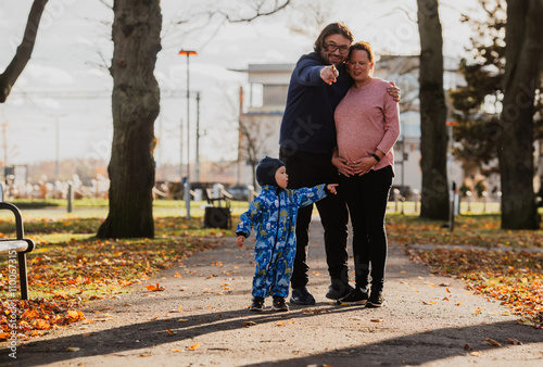 A loving couple strolls through a sunlit park with their young son, surrounded by the vibrant colors of autumn, enjoying a joyful and peaceful family moment together. photo