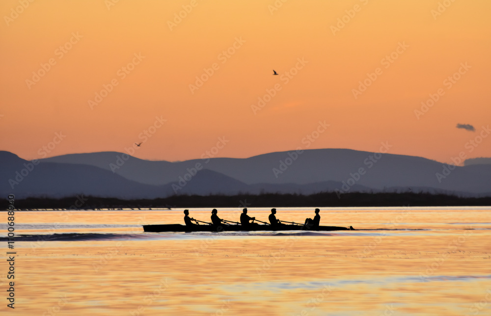Silhouette of persons rowing on a boat at sunset