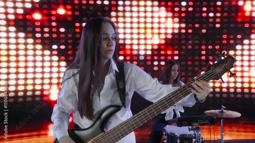 Young female musician is playing the bass guitar on a stage with a colorful led backdrop, creating a vibrant and energetic performance atmosphere