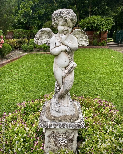 Image of a small Cupid statue with white wings in a nature park.