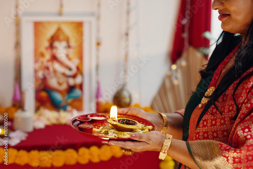 Woman holding plate with traditional items during Ganesh festival celebration. Bright decorations and a Ganesh figure can be seen in the background creating a festive atmosphere photo