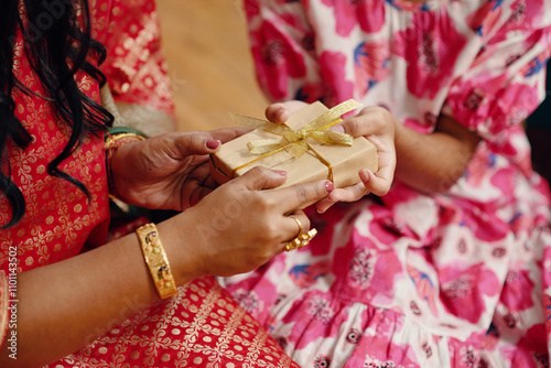 Close-up of two hands exchanging a small gift wrapped in gold ribbon during festive occasion. Individual wearing traditional attire with henna designs on hand photo