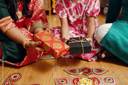 Hands holding beautifully wrapped presents during lively cultural event with intricate decorations on wooden floor, showcasing rich tradition and colorful festive attire photo