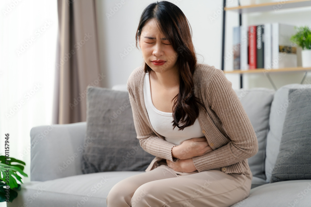 A woman is sitting on a couch holding her stomach with a stomach ache. Healthcare and medical. A woman is sitting on a couch holding her stomach with a stomach ache. Healthcare and medical.