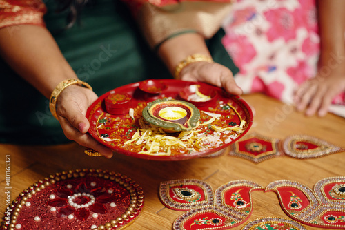 Hands holding beautifully decorated plate adorned with traditional Indian patterns and intricate designs. Surrounding area features more ornate decorations and embellishments photo