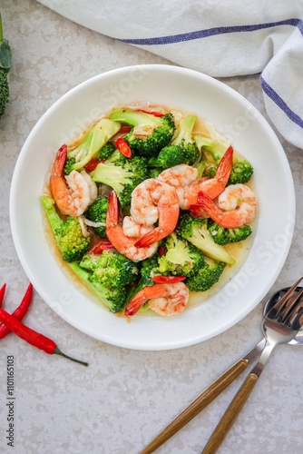 Homemade Stir fried broccoli with shrimp in a white ceramic plate witn spoon and fork on cement background