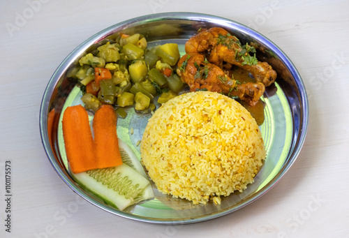 Bhuna khichuri or fried rice with chicken leg pieces, vegetables, and salad, served on a steel plate on a wooden surface. photo