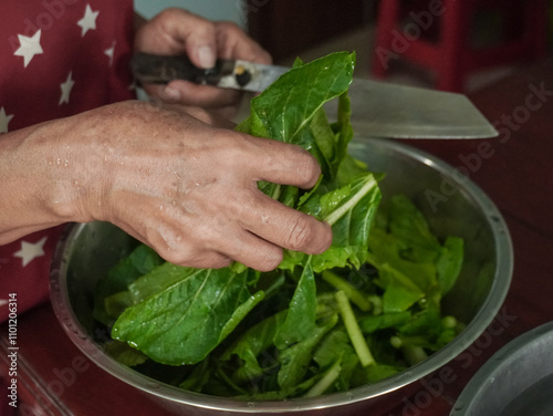 A woman's hand is crushing vegetables in a bowl in the kitchen. Green vegetables that give a fresh feeling, are free from toxic substances, and help nourish the body. Vegetables washing, herbs.  photo