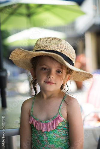 young girl in bathing suit and straw hat looking at camera photo