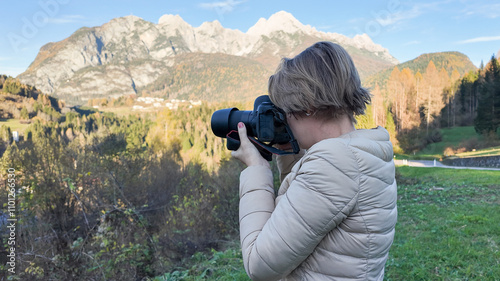 A Caucasian woman captures a scenic mountain landscape with her camera, symbolizing nature photography and exploration during autumn adventures