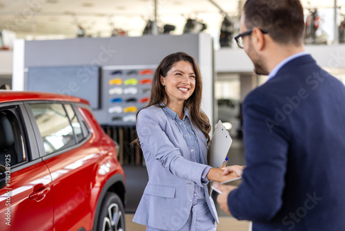 Car dealership manager helps a client choose a car. sales manager selling electric car to a female customer at showroom. Beautiful Caucasian female client customer choosing new car. photo