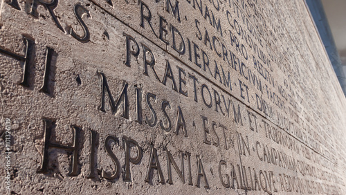 Ancient Roman inscription in Latin (The Deeds of the Divine Augustus, historical document of Roman Empire) carved into stone. Close-up, shallow depth. Public space. Rome, Italy photo