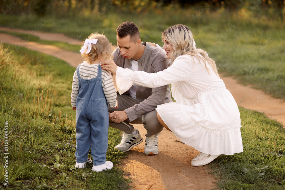 Fototapeta premium A young family with a toddler (around 2 years old) enjoys a moment in nature, smiling and blowing on dandelions. Perfect for concepts of family love, bonding, and childhood memories.
