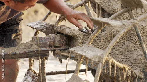 A farmer securing farm tool on muddy hand tractor in waterlogged field photo