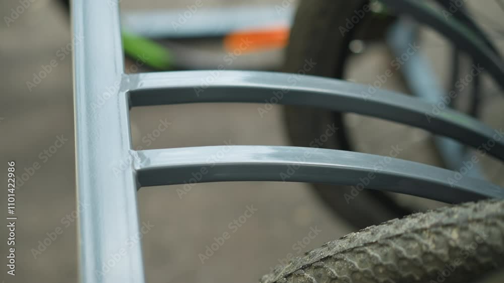 Close-up of bicycle tire secured in metal bike rack with focus on textured wheel and metal frame, background shows another blurred bicycle parked nearby Close-up of bicycle tire secured in metal bike rack with focus on textured wheel and metal frame, background shows another blurred bicycle parked nearby