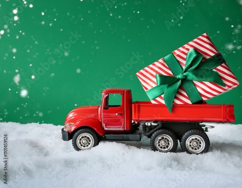 A red toy truck carrying a striped gift box with a green bow moves through snow photo