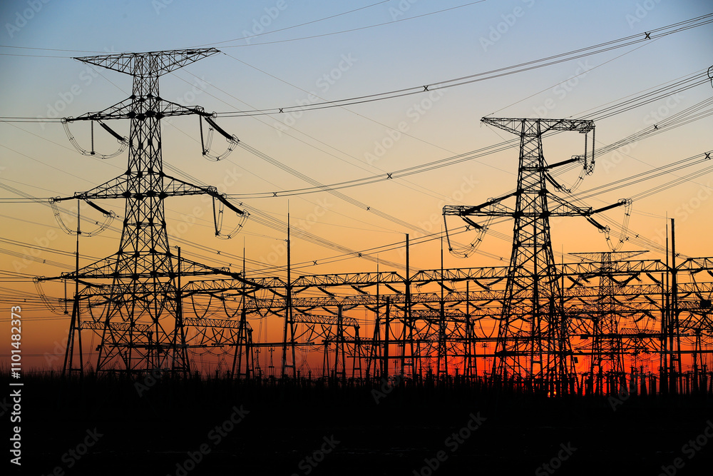 Fototapeta premium Many high-voltage power towers, silhouetted against the setting sun
