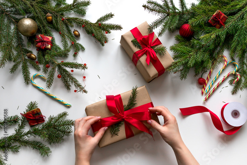 Christmas gift wrapping using eco-friendly materials and pine branches. Tying a gift box with a red ribbon