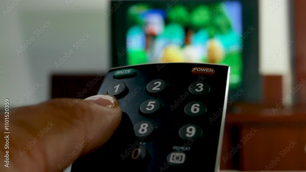The hand holds the TV remote control and switches channels. A person who watches TV at home and switches channels. The hand holds the TV remote control and switches channels. A person who watches TV at home and switches channels.