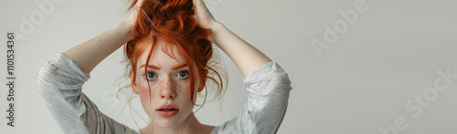 emotional red-haired girl holds her hands near her head on isolated light background