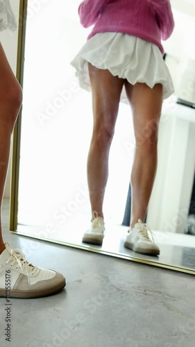 A stylish reflection shot featuring white and beige sneakers, bare legs, and a pink sweater with a white skirt. The healthy, smooth legs highlight fitness and wellness, free from varicose veins, promo photo