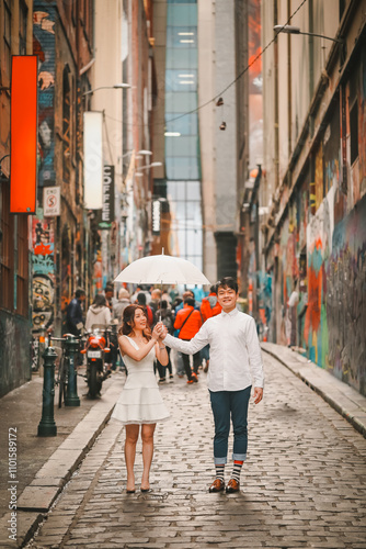 Young engaged couple posing with white umbrella in Hosier Lane, iconic graffiti laneway in Melbourne