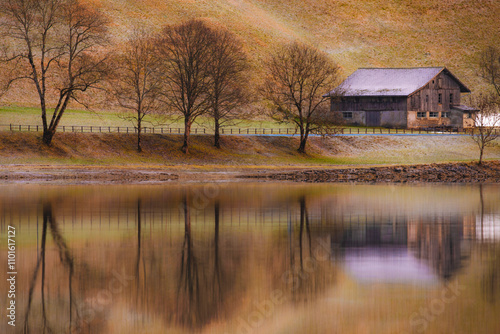 A rustic cabin nestled by a serene lake, surrounded by autumnal trees, reflecting beautifully on the water, evoking calm and nature's majesty. photo