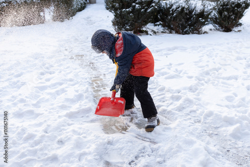 An unrecognizable young boy clears the sidewalk, yard from snow after a strong snowstorm, holding a snow shovel. Winter season, bad weather, cold, snowy