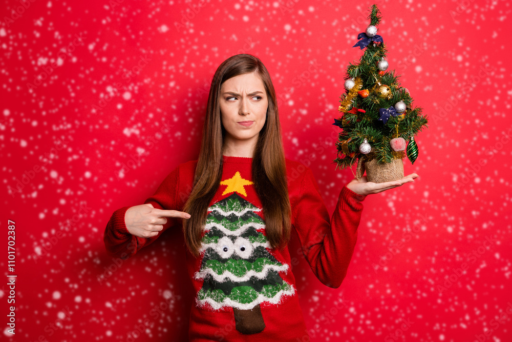 Photo of sad millennial lady point holiday sweater hold look little tree isolated on red color background Photo of sad millennial lady point holiday sweater hold look little tree isolated on red color background
