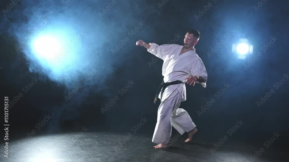 Strong man fighter in white kimono for karate martial arts with black belt preparing for fight training in black background. Man training moves kicks practicing shadow fight ready for sparring Strong man fighter in white kimono for karate martial arts with black belt preparing for fight training in black background. Man training moves kicks practicing shadow fight ready for sparring